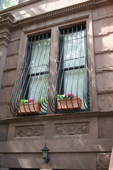 A curved window grill with plants. Window and brown wall in the background. 