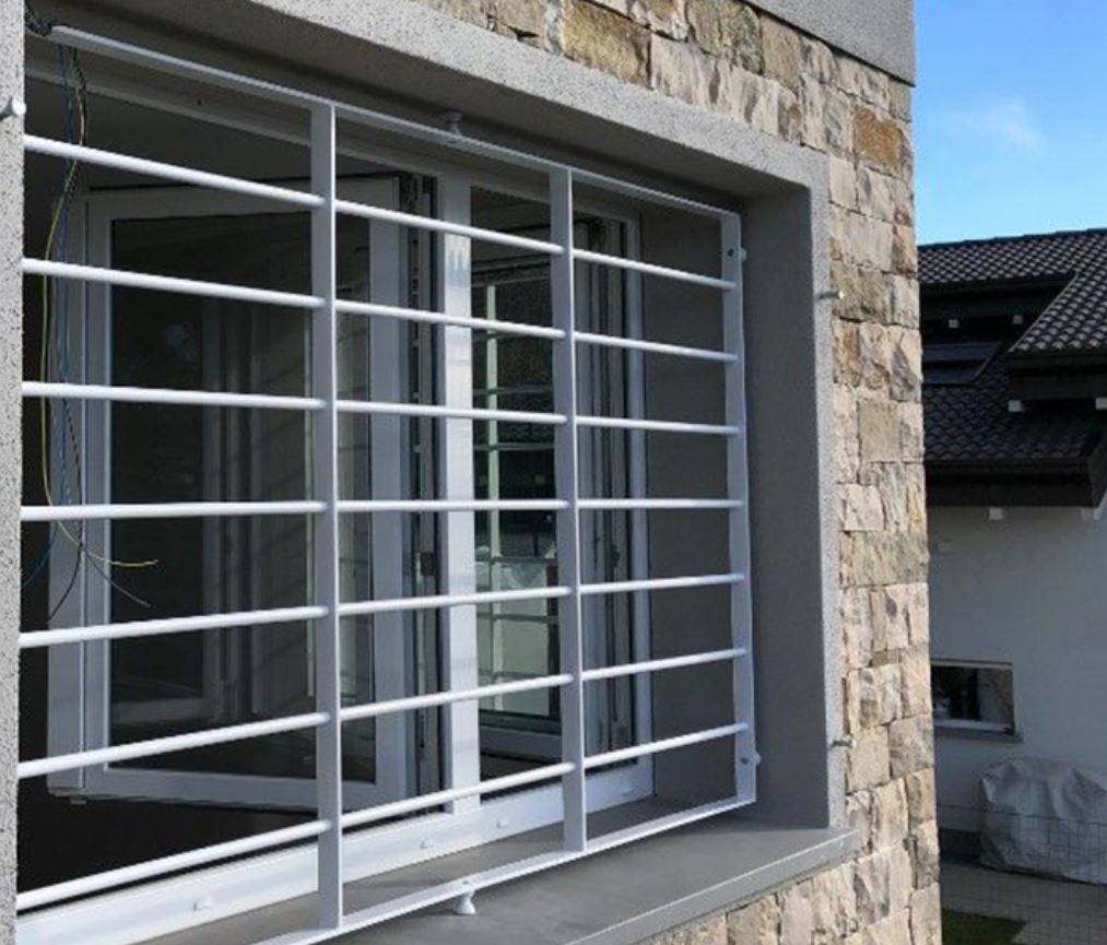 A window with white bars over it. Stone wall and white walls in the background. 