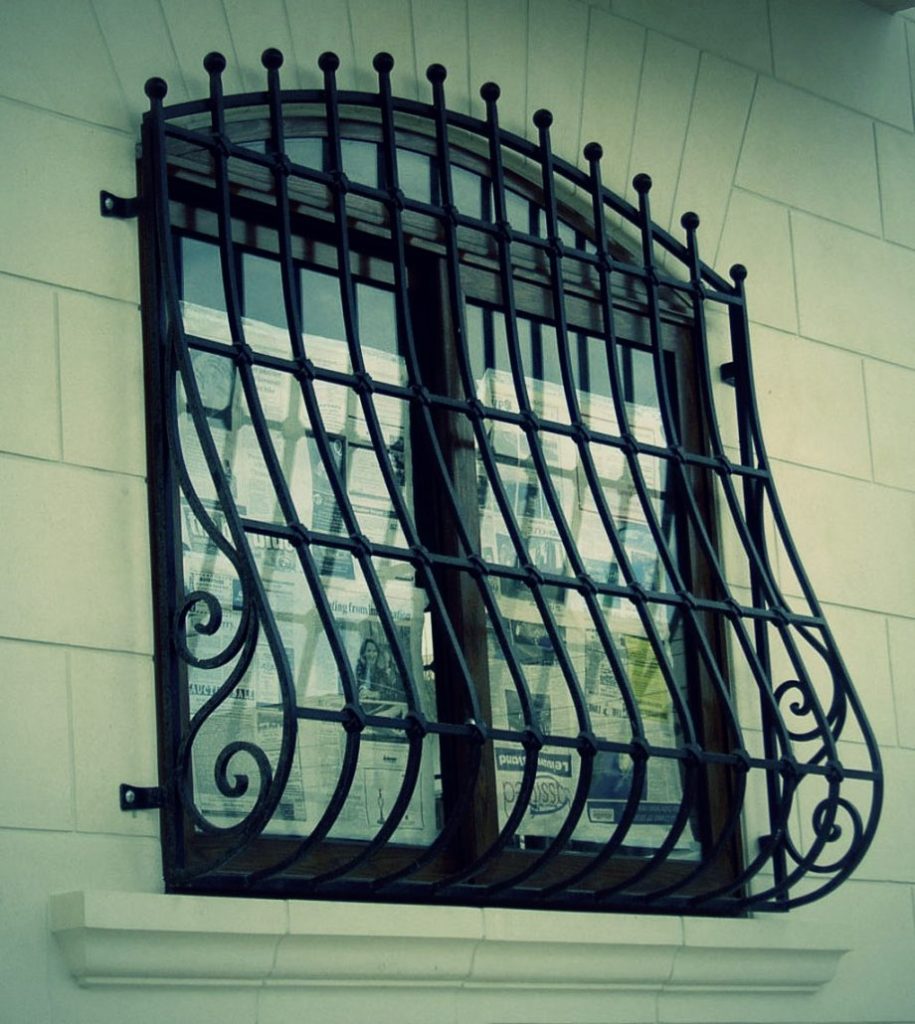 A window with a "potbellied" metal grill. White wall and newspaper in the background. 