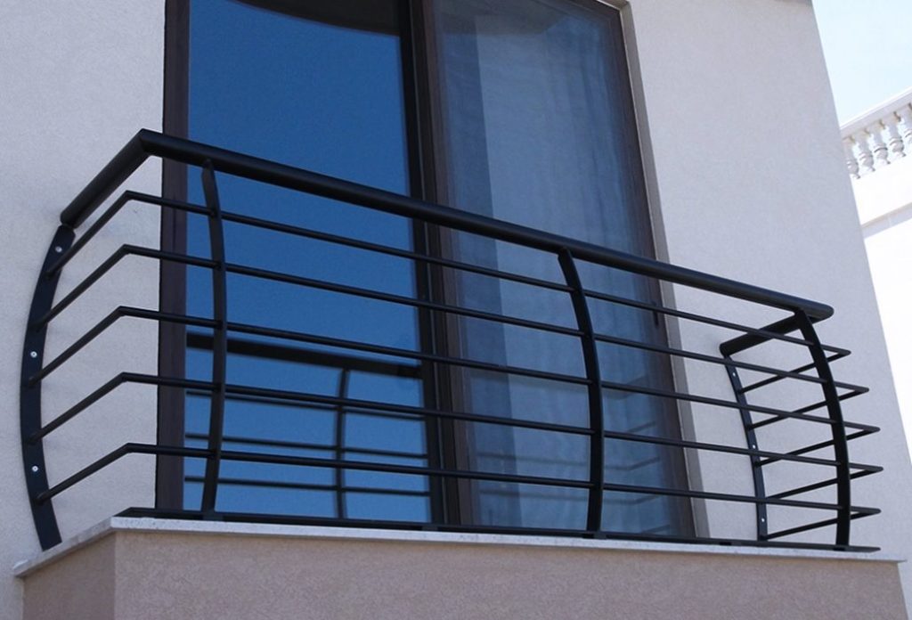 A balcony with bars and a glass door. Curtains and white walls in the background. 